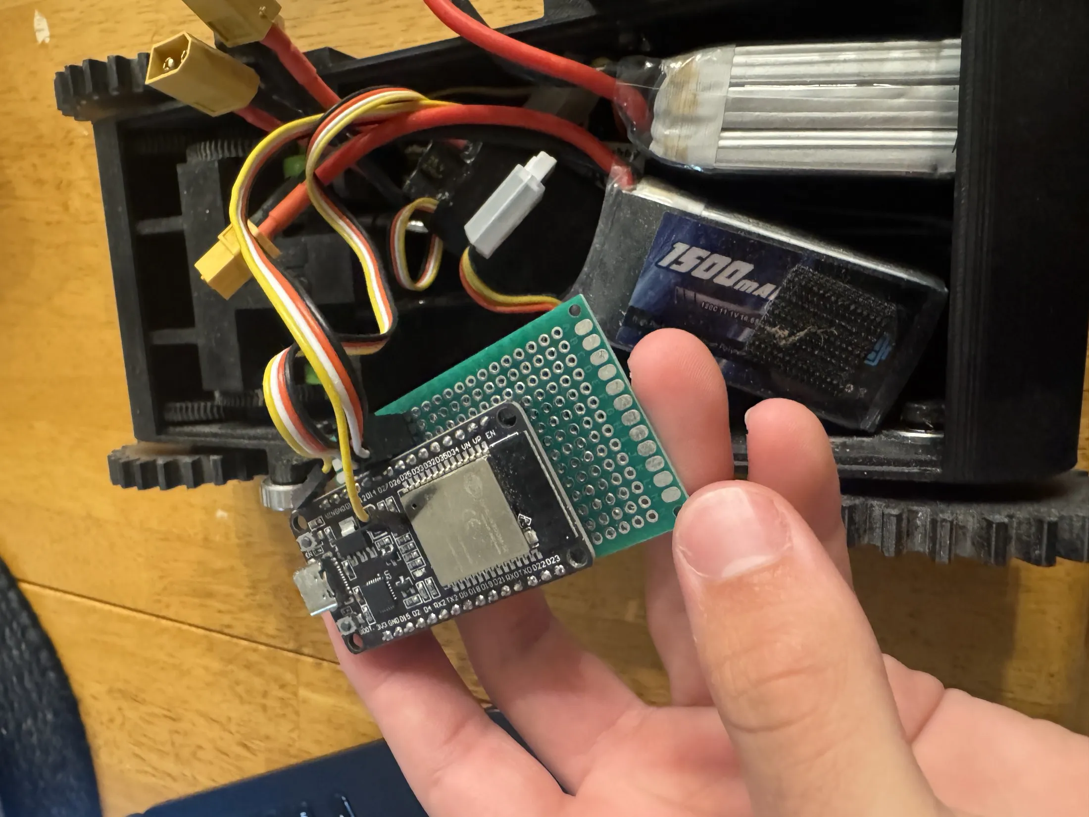 Close-up inside the chassis — an ESP32 dev board on protoboard wired to the ESCs, with a LiPo battery and XT connectors.