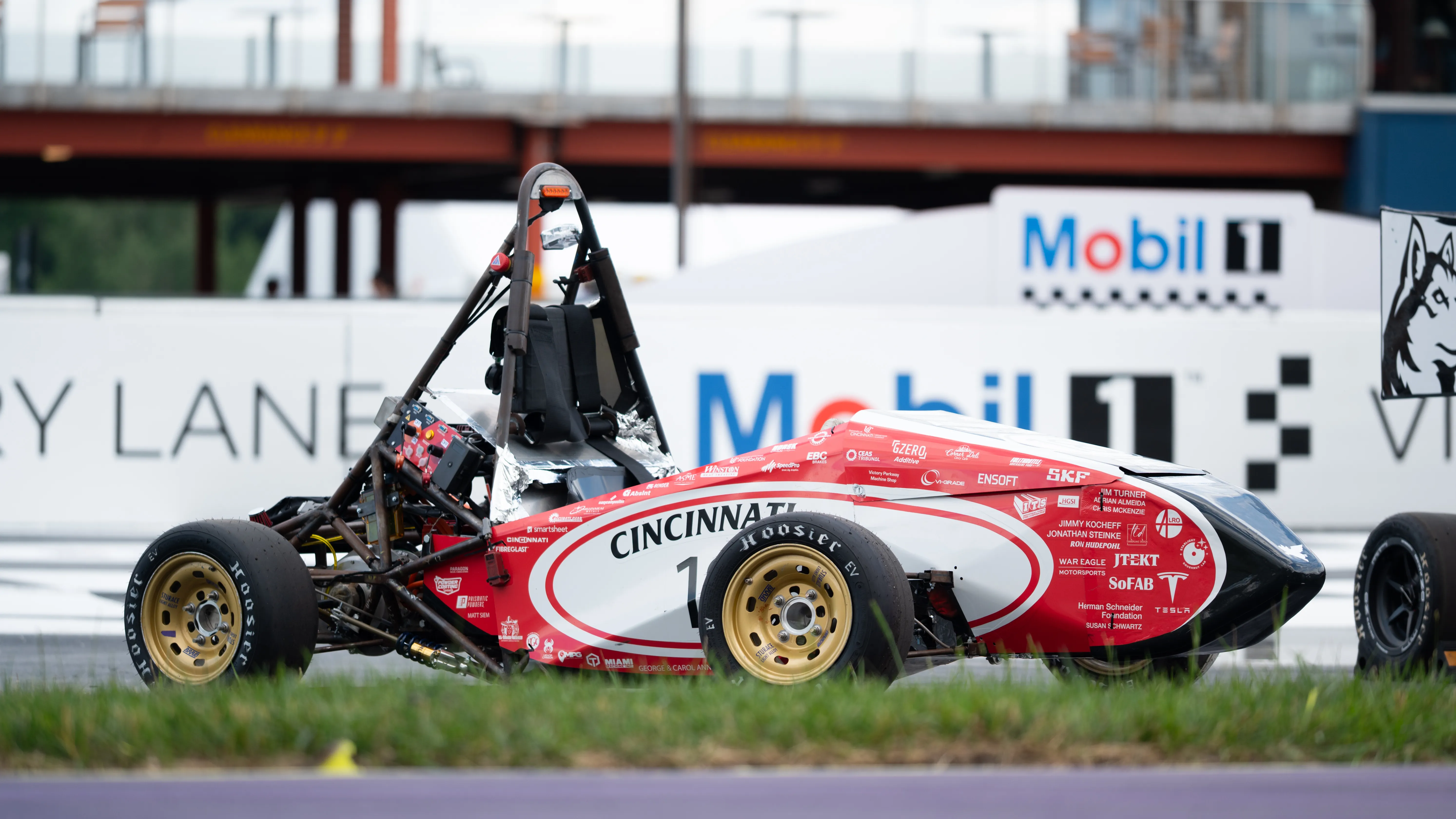Bearcats Electric Racing's EV4 on track — Formula SAE electric car in red-white-and-black Cincinnati livery on gold wheels and Hoosier EV slicks.