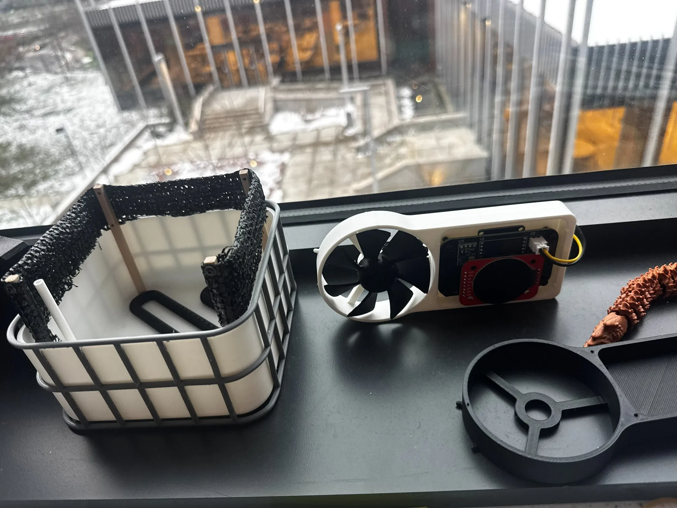 The finished project on a windowsill — the 3D-printed microfarm with black wind mesh on its frame, and the printed anemometer beside it.