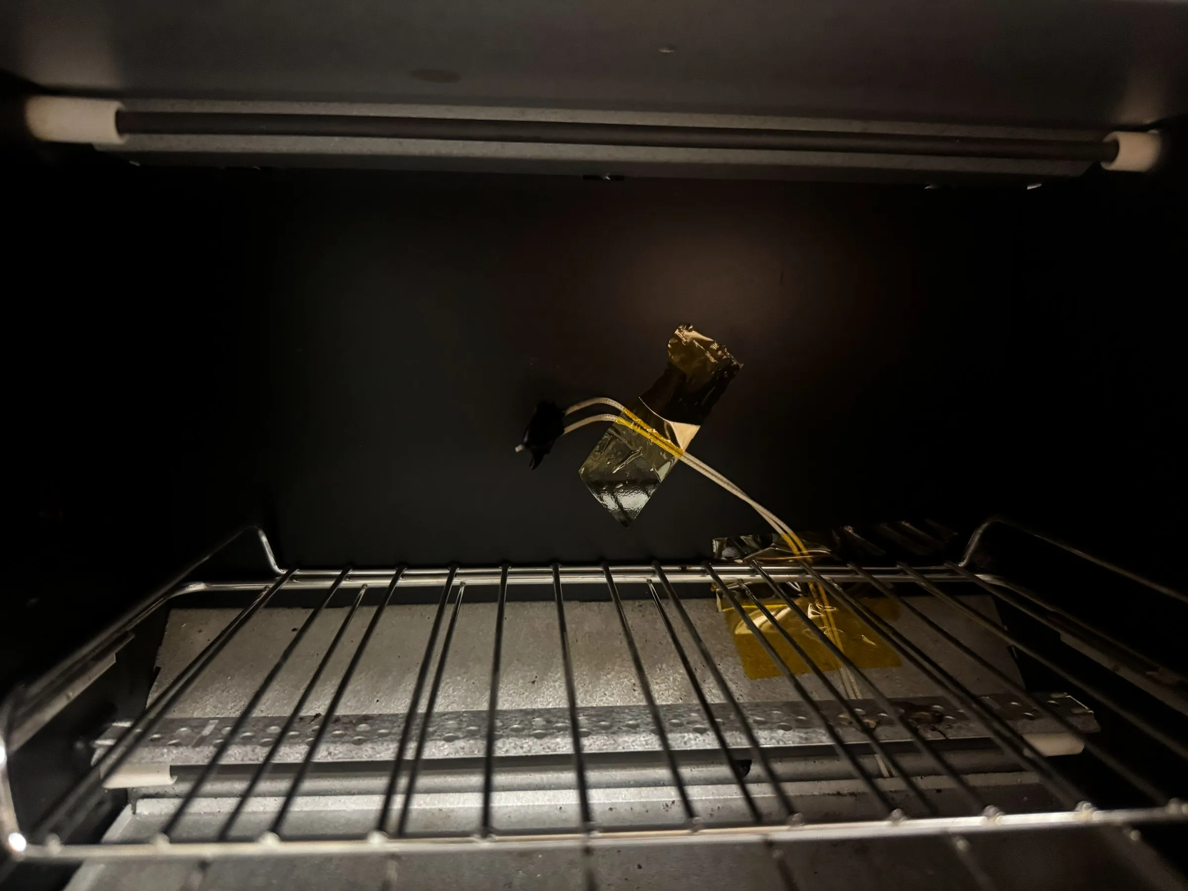 Inside the oven, a thermocouple held in place with Kapton tape through the rear wall, sitting just above the wire rack under the quartz element.